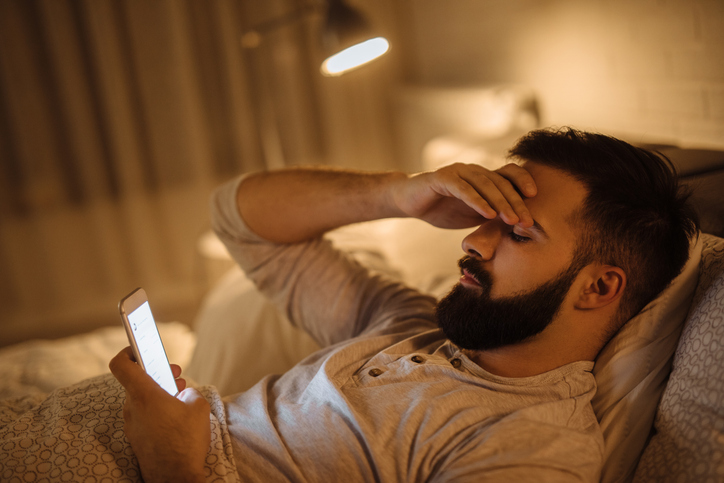 Man ligt op bed en kijkt op zijn telefoon